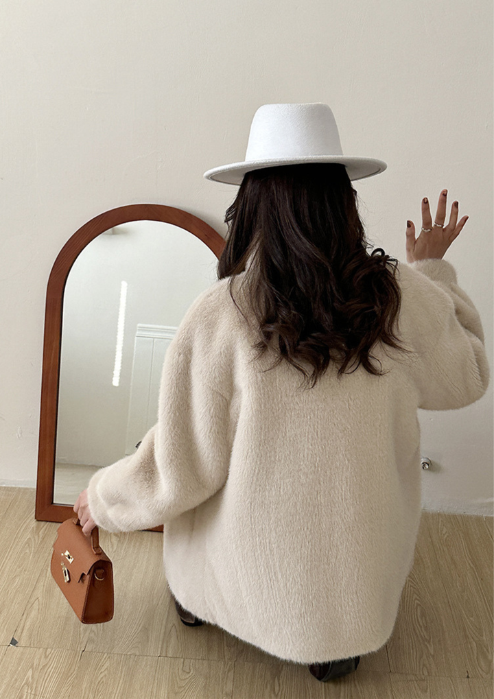 lily Mila plush mink fur coat in cream worn by a woman with a white fedora and brown handbag facing a mirror
